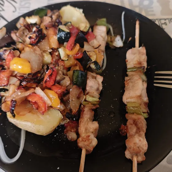 Pinchos de pollo con verduras salteadas, servidos en un plato de pizarra sobre el mantel de papel de un bar