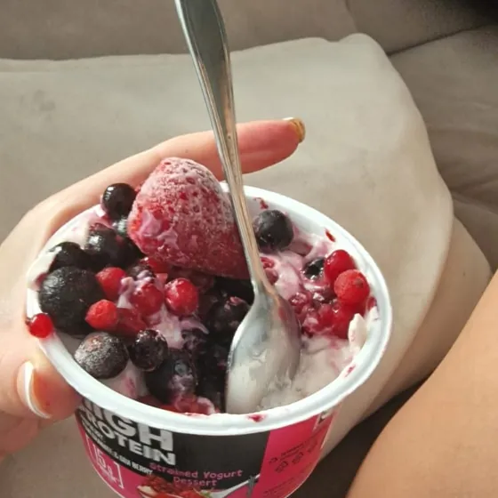 Tarrina de yogur proteico con frutos rojos congelados, comida en el sofá