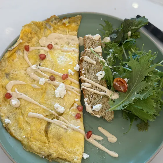 Tortilla francesa con granada, queso de cabra y hojas verdes, en un plato de restaurante