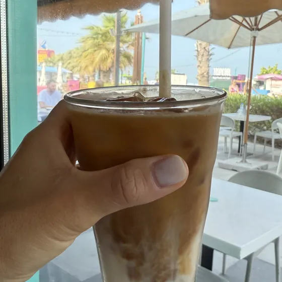 Café con hielo en la mano, en la terraza de una cafetería con sombrillas y palmeras