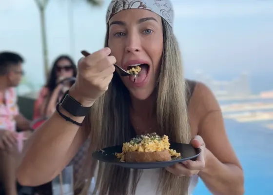 Cristina comiendo un plato en el regazo, con el mar detrás